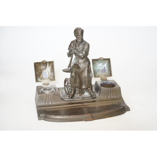 343 - A WMF style spelter Industry inkstand, figure with tools and an anvil, hinged ink wells either sid... 