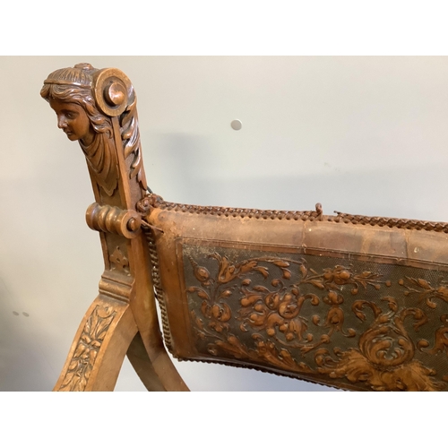 1102 - Two continental carved x-framed elbow chairs, each with tooled leather backs and carved terminals, l... 