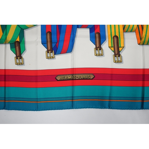 1045 - A Hermès Les Sangles silk scarf, with belt and buckle pattern in hues of white, red, blue, green, an... 