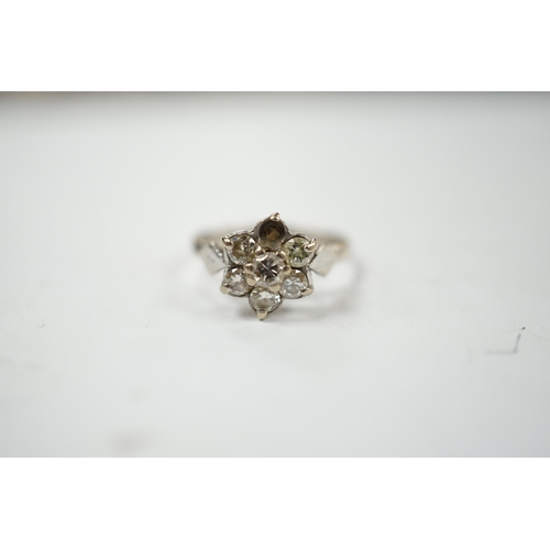 910 - An 18ct white metal and seven stone diamond cluster set flower head ring (one stone missing), size K... 