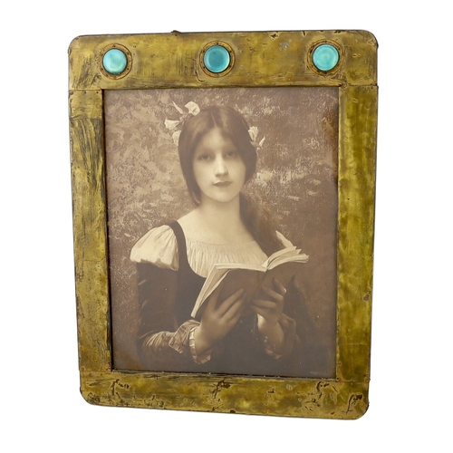 48 - An Arts & Crafts brass picture frame, of rounded rectangular form, the top inset with three turquois... 