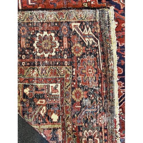 190 - An antique Heriz carpet, with central medallion on a brick red ground, multi bordered, 410 x 295cm... 