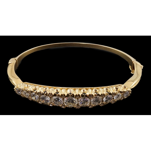 603 - A gold and graduated eleven stone diamond set hinged bangle, with diamond chip spacers, the largest ... 