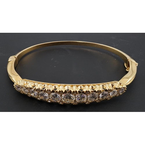 603 - A gold and graduated eleven stone diamond set hinged bangle, with diamond chip spacers, the largest ... 