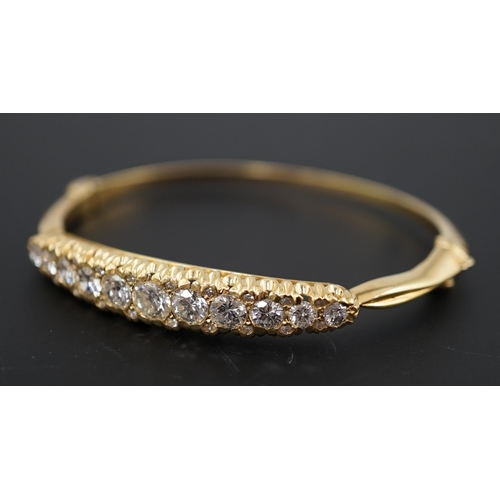 603 - A gold and graduated eleven stone diamond set hinged bangle, with diamond chip spacers, the largest ... 