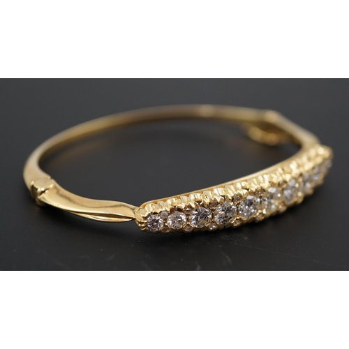 603 - A gold and graduated eleven stone diamond set hinged bangle, with diamond chip spacers, the largest ... 