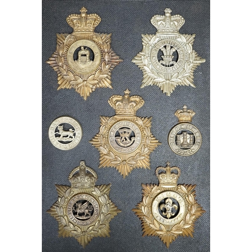 1388 - Five military helmet plates and two other centre badges, mounted on a board including; the Essex Reg... 