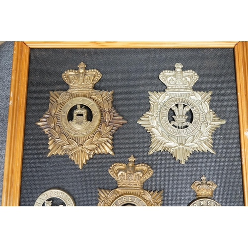 1388 - Five military helmet plates and two other centre badges, mounted on a board including; the Essex Reg... 