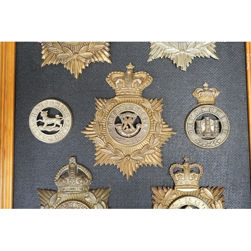 1388 - Five military helmet plates and two other centre badges, mounted on a board including; the Essex Reg... 