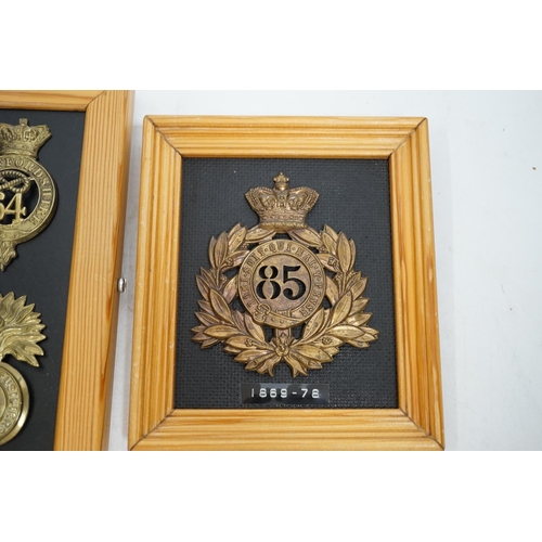 1390 - Five military helmet and shako plates mounted on two boards, including; the Nottinghamshire Regiment... 