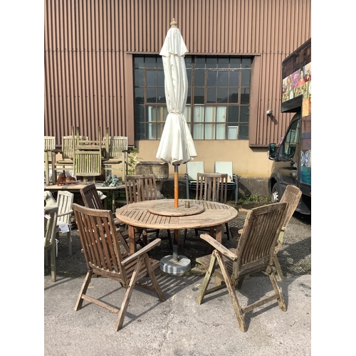 1041 - A circular weathered teak garden table with lazy Susan, diameter 150cm, height 75cm, a crank parasol... 