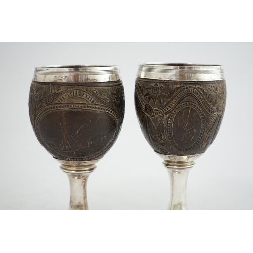 28 - A pair of George III silver mounted coconut cups, maker I.T?, carved with cartouches depicting a pla... 