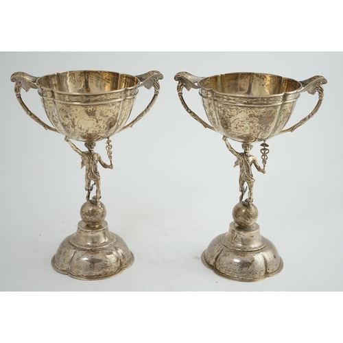 88 - A pair of Victorian silver two handled pedestal cups, each figural stem modelled as Hermes upon a gl... 