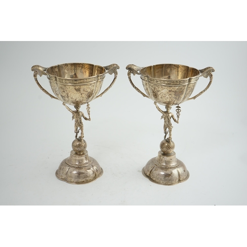 88 - A pair of Victorian silver two handled pedestal cups, each figural stem modelled as Hermes upon a gl... 