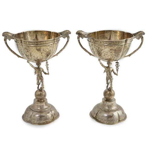 88 - A pair of Victorian silver two handled pedestal cups, each figural stem modelled as Hermes upon a gl... 