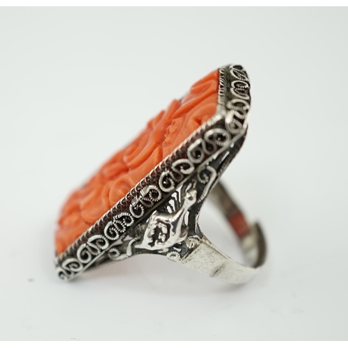 222 - A Chinese carved coral and silver ring, early 20th century, the coral plaque carved and pierced with... 