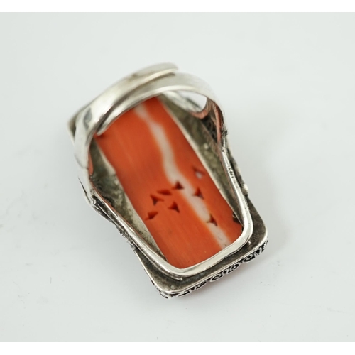 222 - A Chinese carved coral and silver ring, early 20th century, the coral plaque carved and pierced with... 