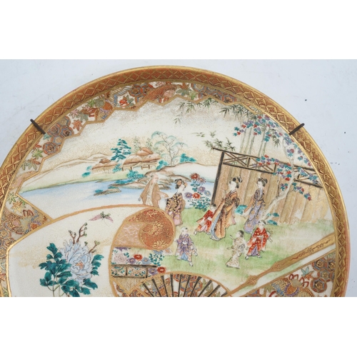 28 - A Japanese Satsuma garden scene dish, Meiji period, painted with figures in a landscape to a fan s... 