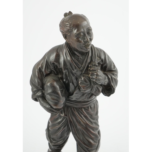 55 - A Japanese bronze figure of a man, 19th century, carrying fabric wrapped packages suspended from str... 