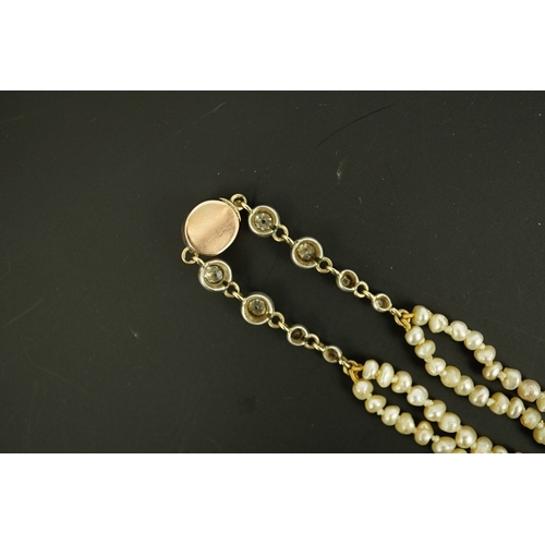 134 - An antique twin strand baroque pearl necklace, with pearl set gold clasp bordered with single chain ... 