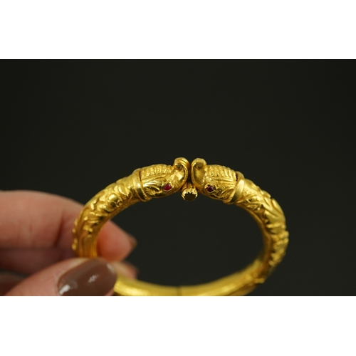 152 - An antique Indian? high carat gold hinged bangle, with elephant head terminals and red stone set eye... 