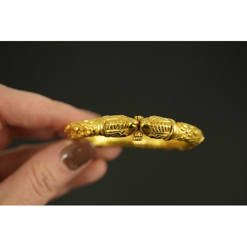 152 - An antique Indian? high carat gold hinged bangle, with elephant head terminals and red stone set eye... 