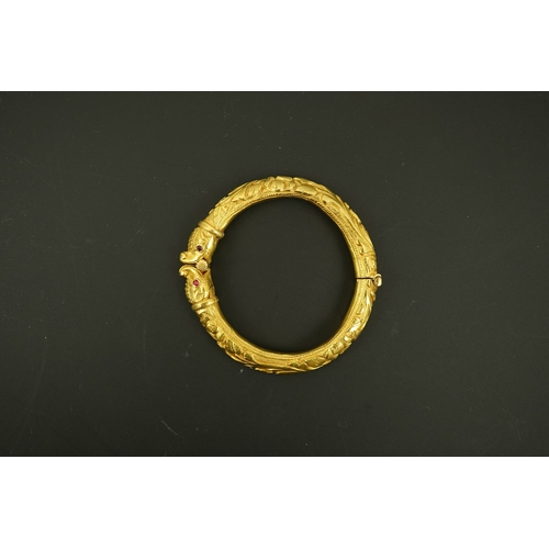 152 - An antique Indian? high carat gold hinged bangle, with elephant head terminals and red stone set eye... 