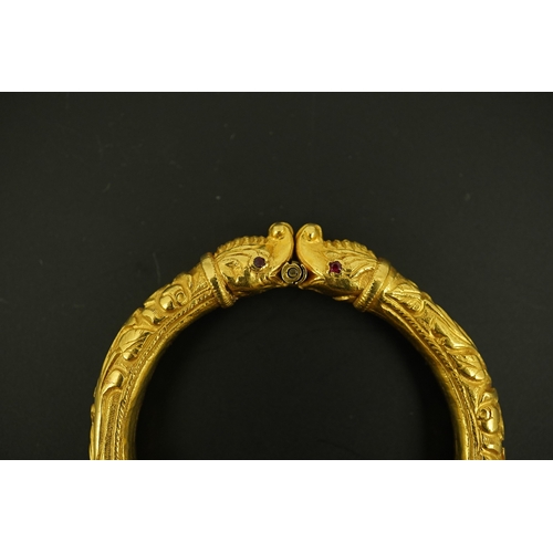 152 - An antique Indian? high carat gold hinged bangle, with elephant head terminals and red stone set eye... 