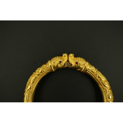 152 - An antique Indian? high carat gold hinged bangle, with elephant head terminals and red stone set eye... 