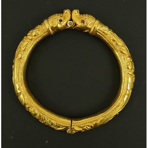 152 - An antique Indian? high carat gold hinged bangle, with elephant head terminals and red stone set eye... 