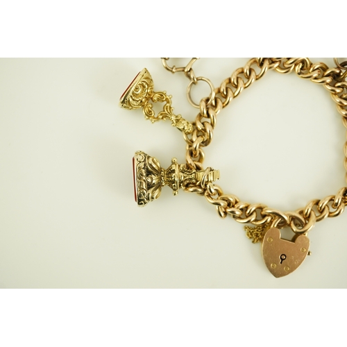 165 - An Edwardian 15ct gold curb link charm bracelet with heart shaped padlock clasp, hung with six assor... 