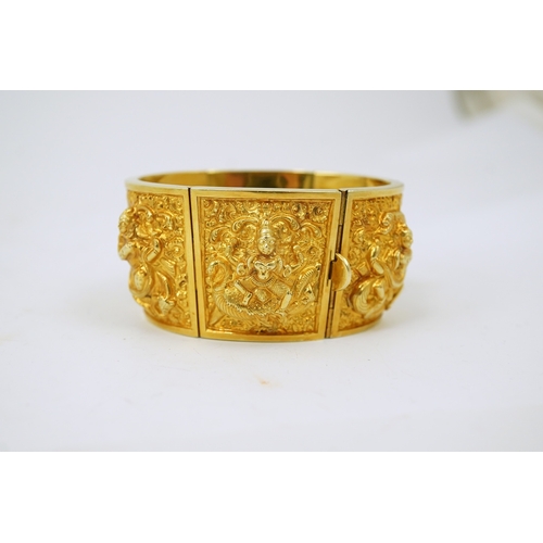 173 - An early 20th century Indian gold hinged panelled cuff bracelet, embossed with deities amongst scrol... 