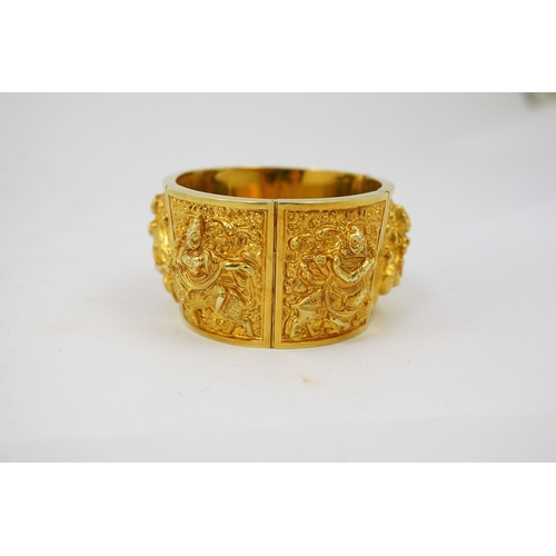 173 - An early 20th century Indian gold hinged panelled cuff bracelet, embossed with deities amongst scrol... 