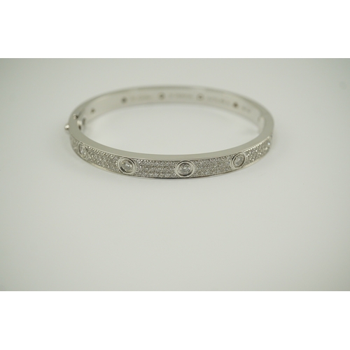 283 - A modern Cartier 18k white gold and diamond cluster set hinged 'Love' bangle, set with twelve interm... 