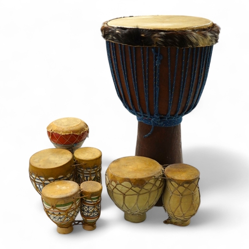 1293 - Five African drums; a Djembe, 60cm high, together with four small North African pottery double drums... 