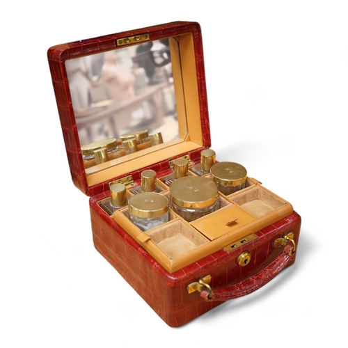 426 - A red stained crocodile skin two layer vanity case, fitted with brass topped bottles and pots, case ... 