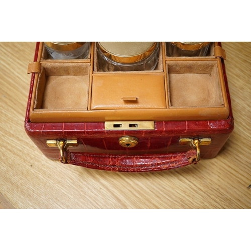 426 - A red stained crocodile skin two layer vanity case, fitted with brass topped bottles and pots, case ... 