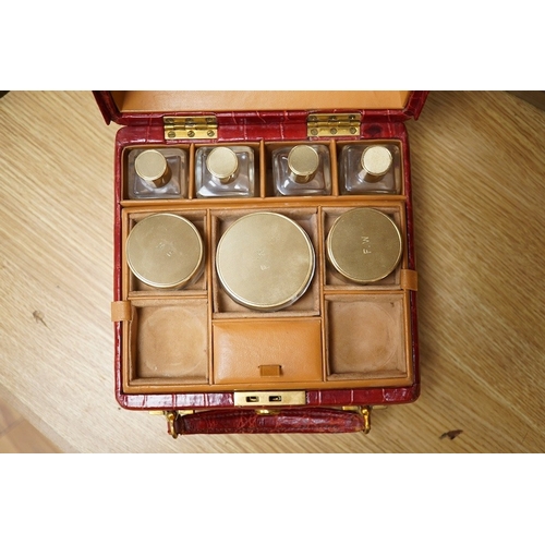 426 - A red stained crocodile skin two layer vanity case, fitted with brass topped bottles and pots, case ... 