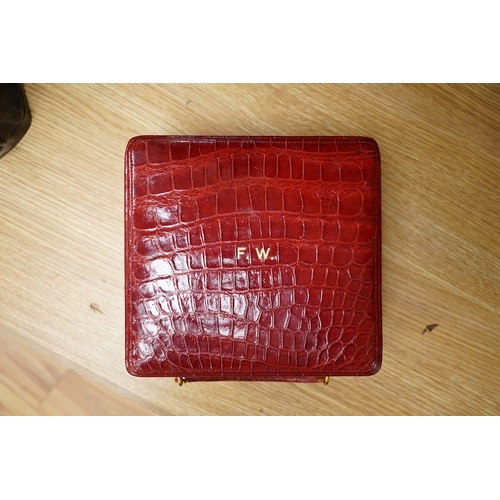 426 - A red stained crocodile skin two layer vanity case, fitted with brass topped bottles and pots, case ... 