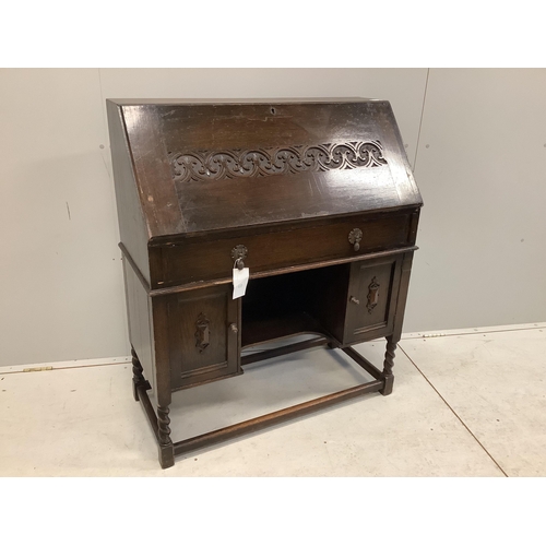 1107 - A dark oak Tudor style bureau with a decorative carved front, single drawer above cupboard doors, wi... 