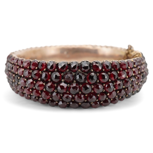 1930 - An Edwardian yellow metal overlaid and facetted garnet cluster set hinged bracelet, with safety chai... 