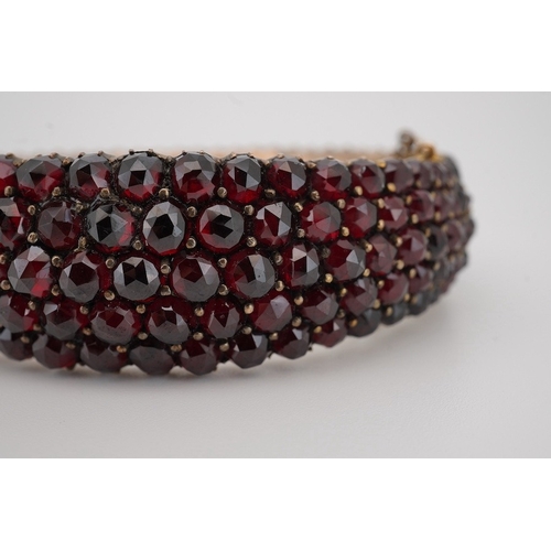 1930 - An Edwardian yellow metal overlaid and facetted garnet cluster set hinged bracelet, with safety chai... 