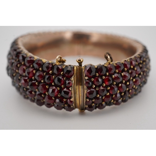 1930 - An Edwardian yellow metal overlaid and facetted garnet cluster set hinged bracelet, with safety chai... 