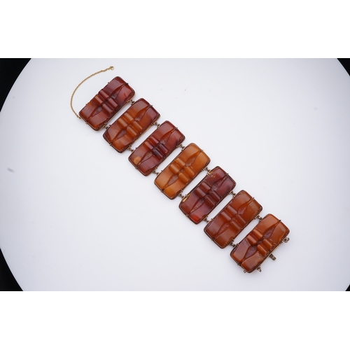 235 - A gold and amber bracelet, composed of panels of amber carved with scroll motifs, mounted in gold, l... 