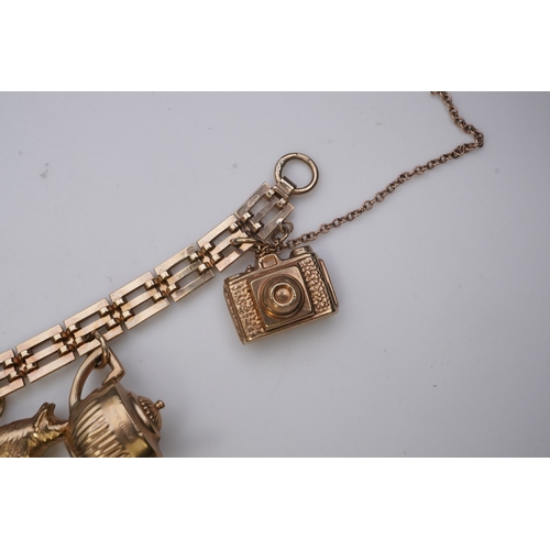 243 - A charm bracelet, mid 20th century, the 9ct gate link bracelet suspending a series of twelve charms ... 