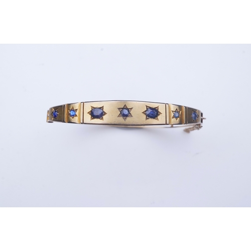 284 - A Victorian sapphire bangle, late 19th century, of hinged design, the front set with a sequence of o... 