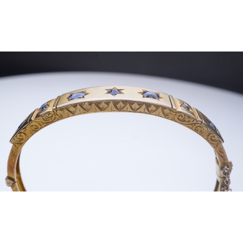 284 - A Victorian sapphire bangle, late 19th century, of hinged design, the front set with a sequence of o... 