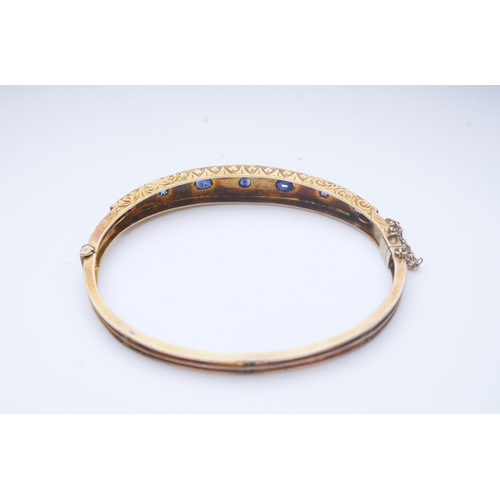 284 - A Victorian sapphire bangle, late 19th century, of hinged design, the front set with a sequence of o... 