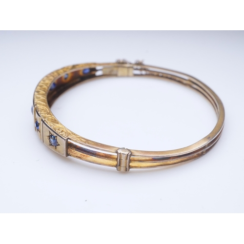 284 - A Victorian sapphire bangle, late 19th century, of hinged design, the front set with a sequence of o... 