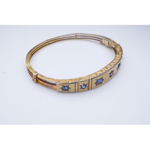 284 - A Victorian sapphire bangle, late 19th century, of hinged design, the front set with a sequence of o... 